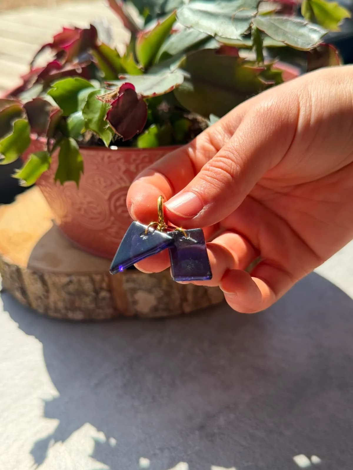Boucles d'oreilles asymétriques en verre violet, triangle et rectangle, sur un rondin de bois