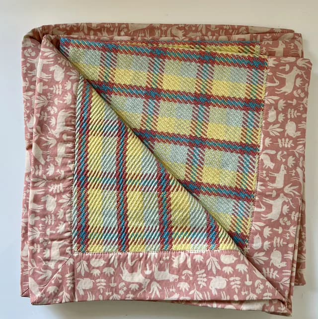 Plaid bébé plié au tissage tartan pastel jaune et bleu avec bordure rose à motifs d'animaux des bois