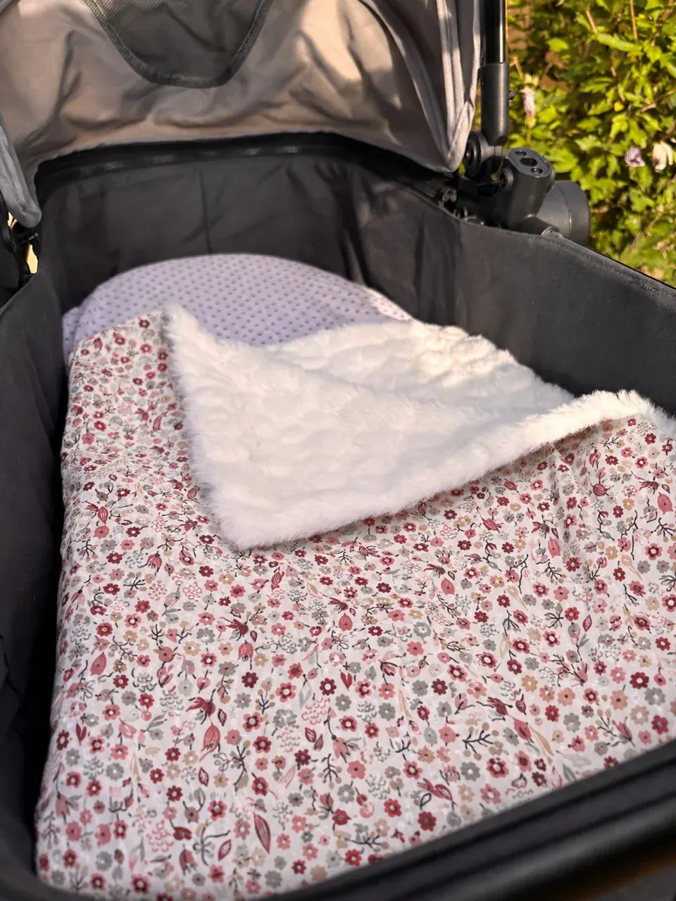 Couverture pour bébé à motif floral posée dans un landau avec revers en polaire texturée blanche.