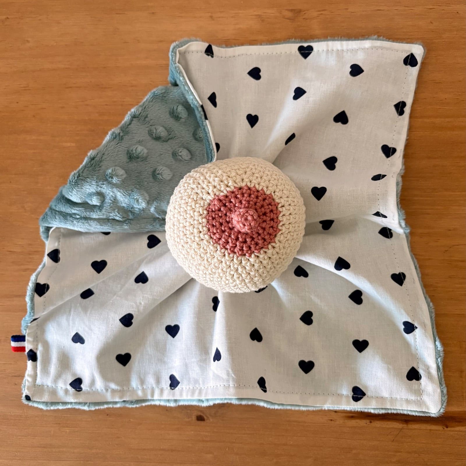 Doudou carré blanc à petits cœurs avec sein en crochet beige et tétine rose, doublé d'un tissu texturé vert