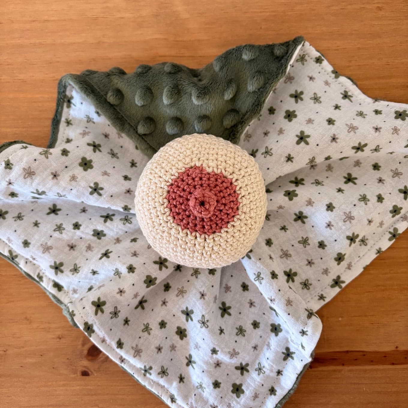 Doudou d'allaitement en crochet beige et rose sur tissu à motifs fleuris et envers vert forêt à pois.