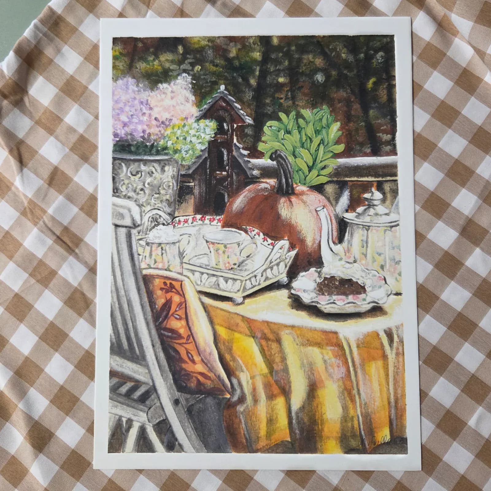 Illustration peinte d'une table d'automne avec citrouille, service à thé et fleurs posée sur un tissu à carreaux.