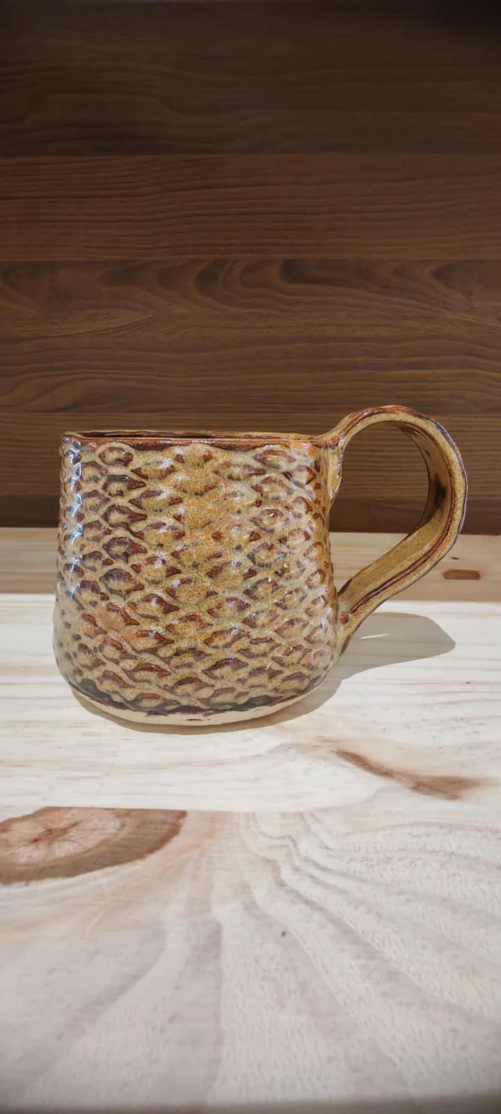 Tasse en céramique marron texturée façon pomme de pin posée sur un support en bois.